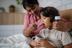 Ill boy taking medicine from his mother at home.